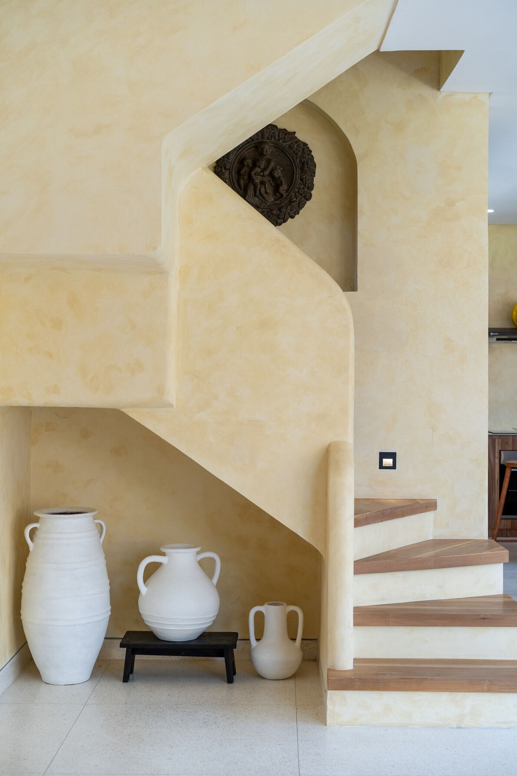 A staircase with a beige wall and a decorative plate. There are three white vases on a small table below the stairs.