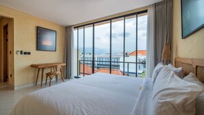 Een hotelkamer met een groot bed, een bureau en uitzicht op gebouwen door grote ramen.