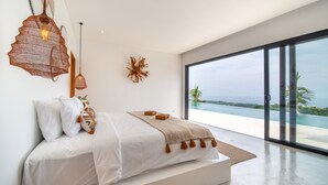 A modern bedroom with a large window, a bed with white linens, a hanging light fixture, and a decorative wall piece. - Infinity Pool | Private Wellness Space | Sea Views (Lovina)