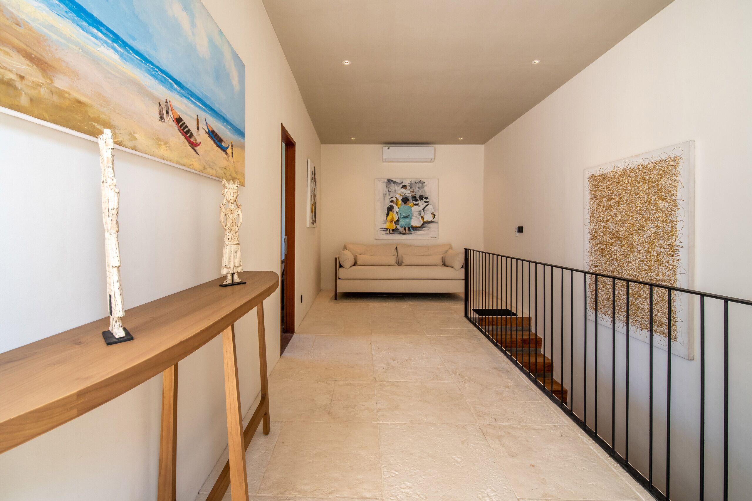 Un couloir avec une console en bois, un canapé beige et un escalier doté d’une rampe noire.