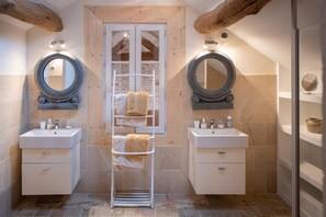 Un bagno con due lavandini, due ampi specchi, un portascopevoli e una finestra con travi in legno.