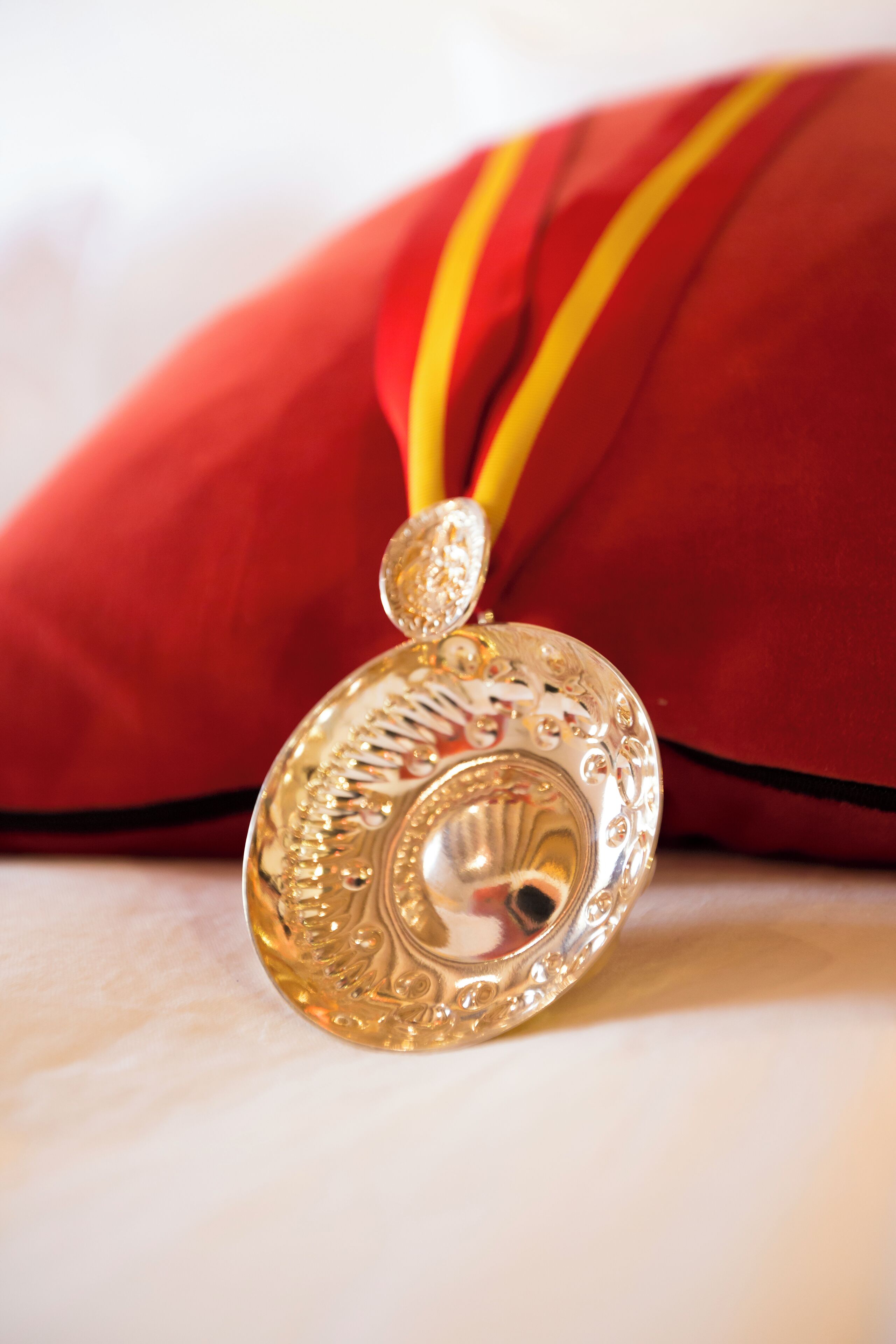 A gold pendant with intricate designs, resting on a red cushion with a yellow ribbon.