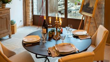 Une table à manger dressée avec des assiettes, des verres et des bougies, entourée de chaises rembourrées.