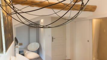 A modern bedroom with a geometric light fixture, a large bed with pillows, and a visible bathroom in the background.