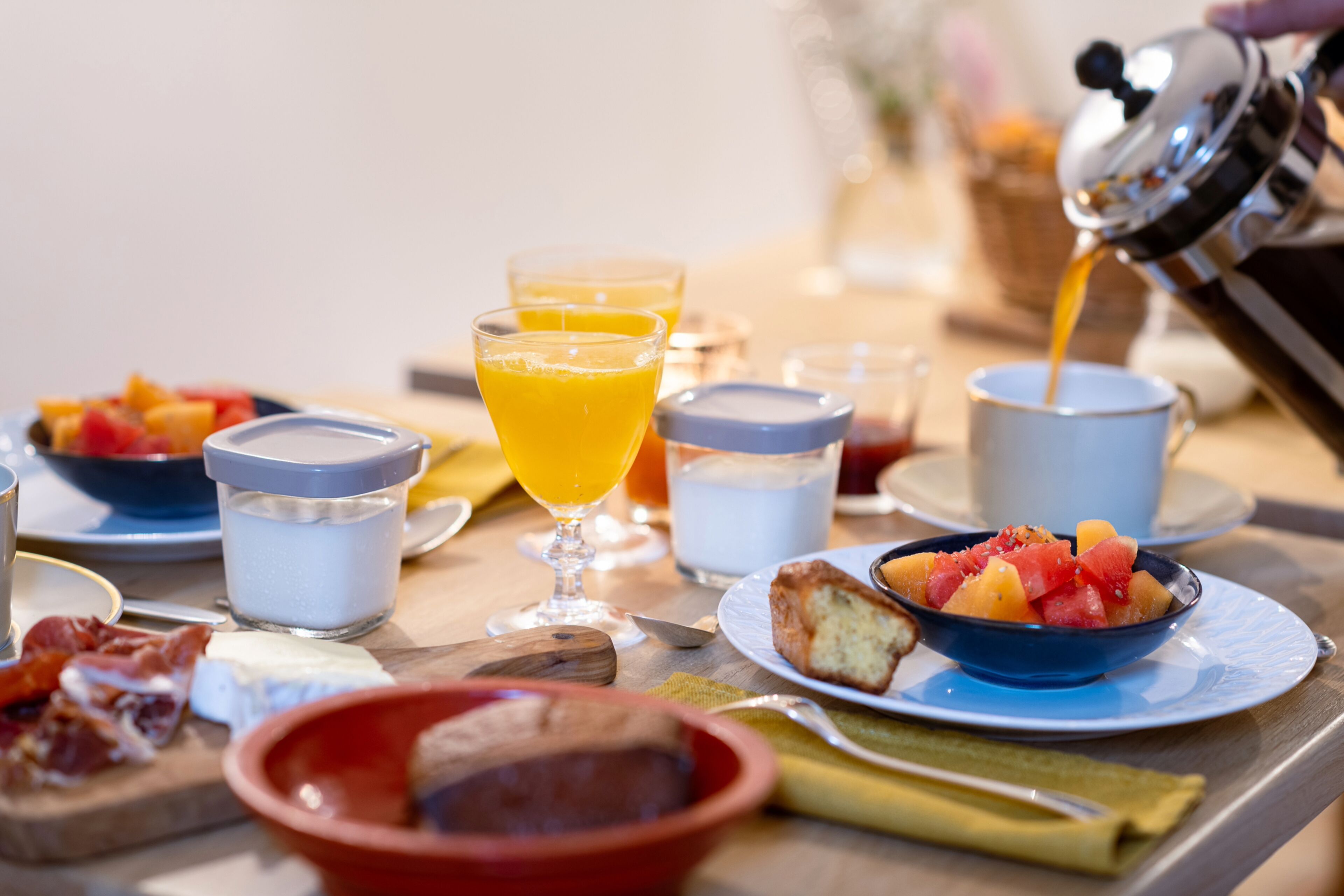 Une table de petit-déjeuner avec divers aliments et boissons, notamment une cafetière versant du café dans une tasse.