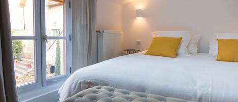 Un dormitorio con cama, ventana con cortinas, radiador y una lámpara fijada a la pared.