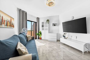 Uma sala de estar moderna com um sofá, uma televisão de tela plana, um rack branco e uma pintura com vista para a cidade.