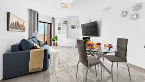 Una sala de estar moderna con un sofá, una mesa de comedor con sillas, un televisor montado en la pared y una pintura de un paisaje urbano.