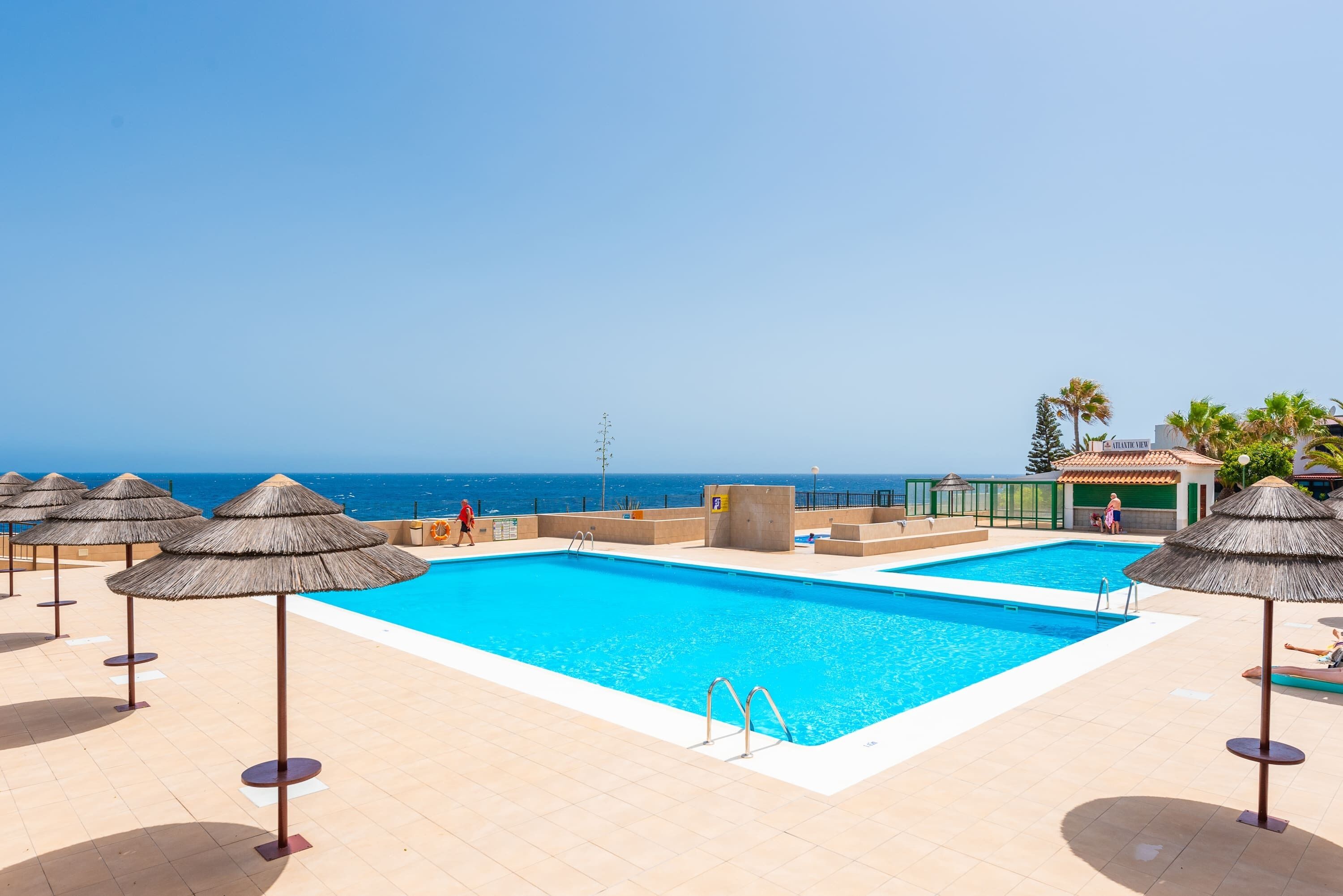 Ein Poolbereich mit zwei Schwimmbecken, Liegestühlen und Sonnenschirmen.