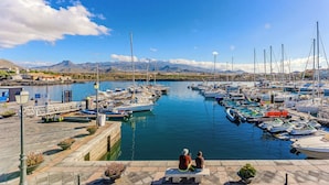 Un puerto deportivo con barcos amarrados, cielo despejado y montañas al fondo.