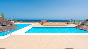 Zona de piscina con vista al mar, un puesto de socorrista y una estructura con techo de paja.