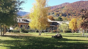 A traditional building with a tiled roof, surrounded by a grassy area with trees displaying autumn foliage. - Hotel Cocoon (Pescasseroli)