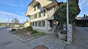 En tvåvåningsbyggnad med en symmetrisk fasad, en central entré med en trappa och en liten trädgårdsyta med en stenlagd gång.