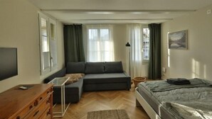 Ett modernt sovrum med en bäddsoffa, en platt-TV, en byrå i trä och en säng med ett grått överkast.