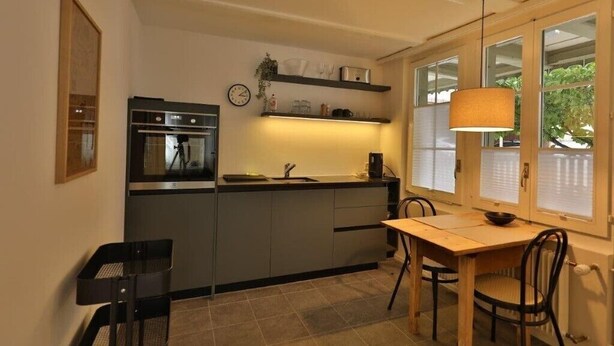Ett kompakt kök med en inbyggd ugn, en diskho och en matplats med ett bord och stolar.