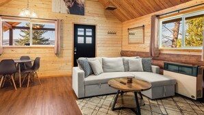 A cozy cabin interior with a wooden ceiling, a sofa, a dining table, and a window with a view of trees. - Adventure Log Cabin with Expansive Views, Discovery Ski Hill nearby, walk to downtown. Perfect for couples and small families! (Philipsburg)