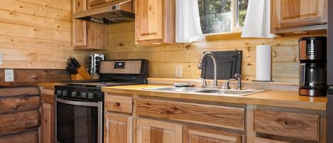 A wooden cabin kitchen with a stove, oven, sink, and a coffee maker.