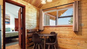 A wooden cabin interior with a dining table and chairs, a bed, and a window with curtains. - Adventure Log Cabin with Expansive Views, Discovery Ski Hill nearby, walk to downtown. Perfect for couples and small families! (Philipsburg)