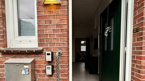 A brick building entrance with a window, a wall-mounted light, a door, and a small utility box. - StadtHOUSE Bentheim – Viel Platz für Gruppen (Bad Bentheim)