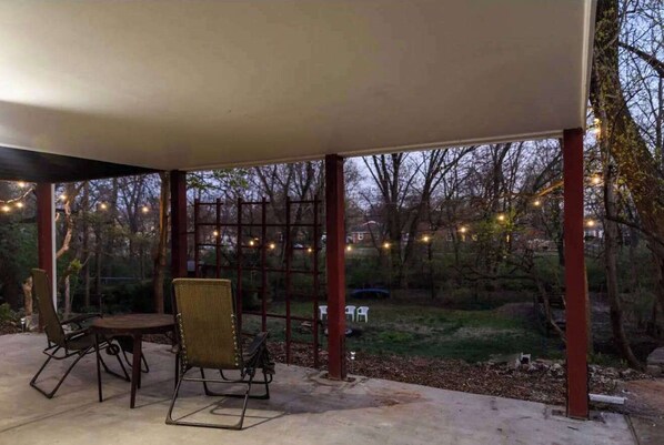 An outdoor patio area with a table and chairs, surrounded by a wooden fence and string lights.