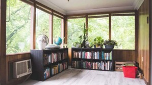 A sunlit reading nook with large windows, bookshelves, and potted plants.