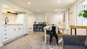 A modern kitchen with white cabinetry, a dining area with a wooden table and chairs, and a staircase leading to another level.