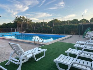 A swimming pool with a blue water feature, surrounded by white lounge chairs and artificial green grass. - El Portachuelo (Sonseca)