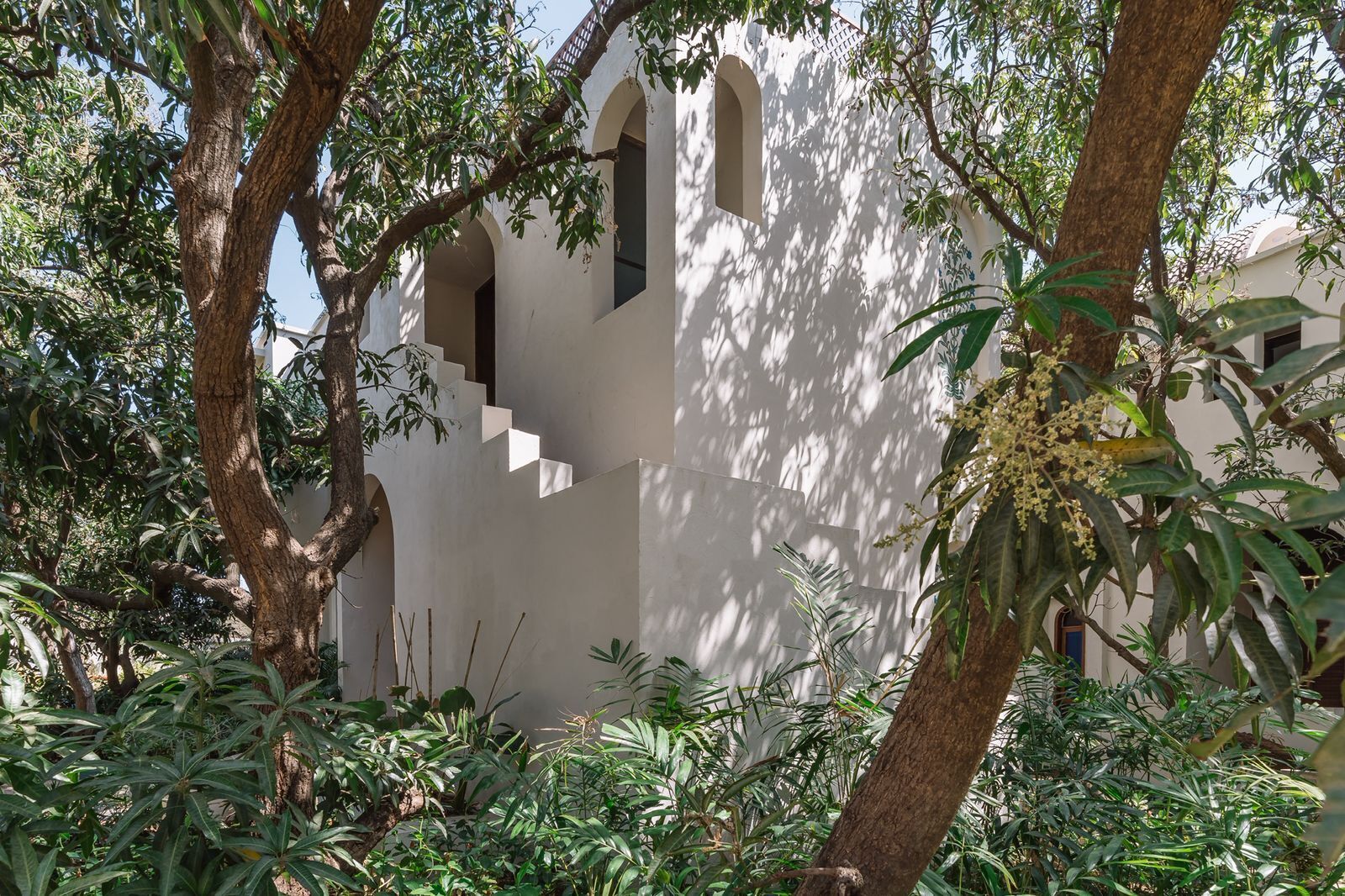 A building with arched windows and a staircase leading to an upper level, surrounded by lush greenery.