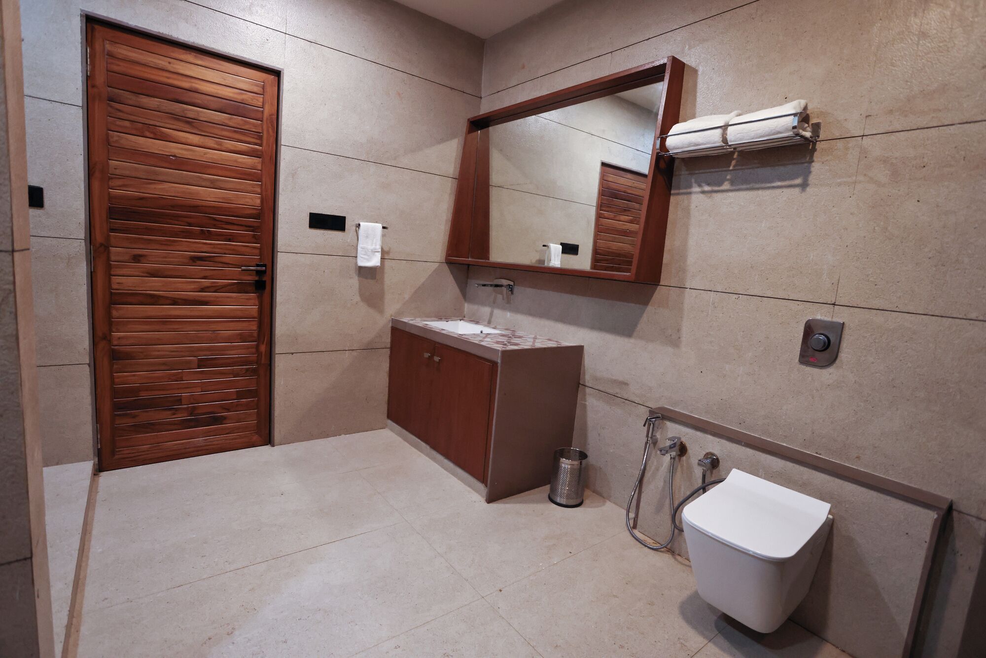 A bathroom with a wooden door, a sink, a mirror, and a toilet.