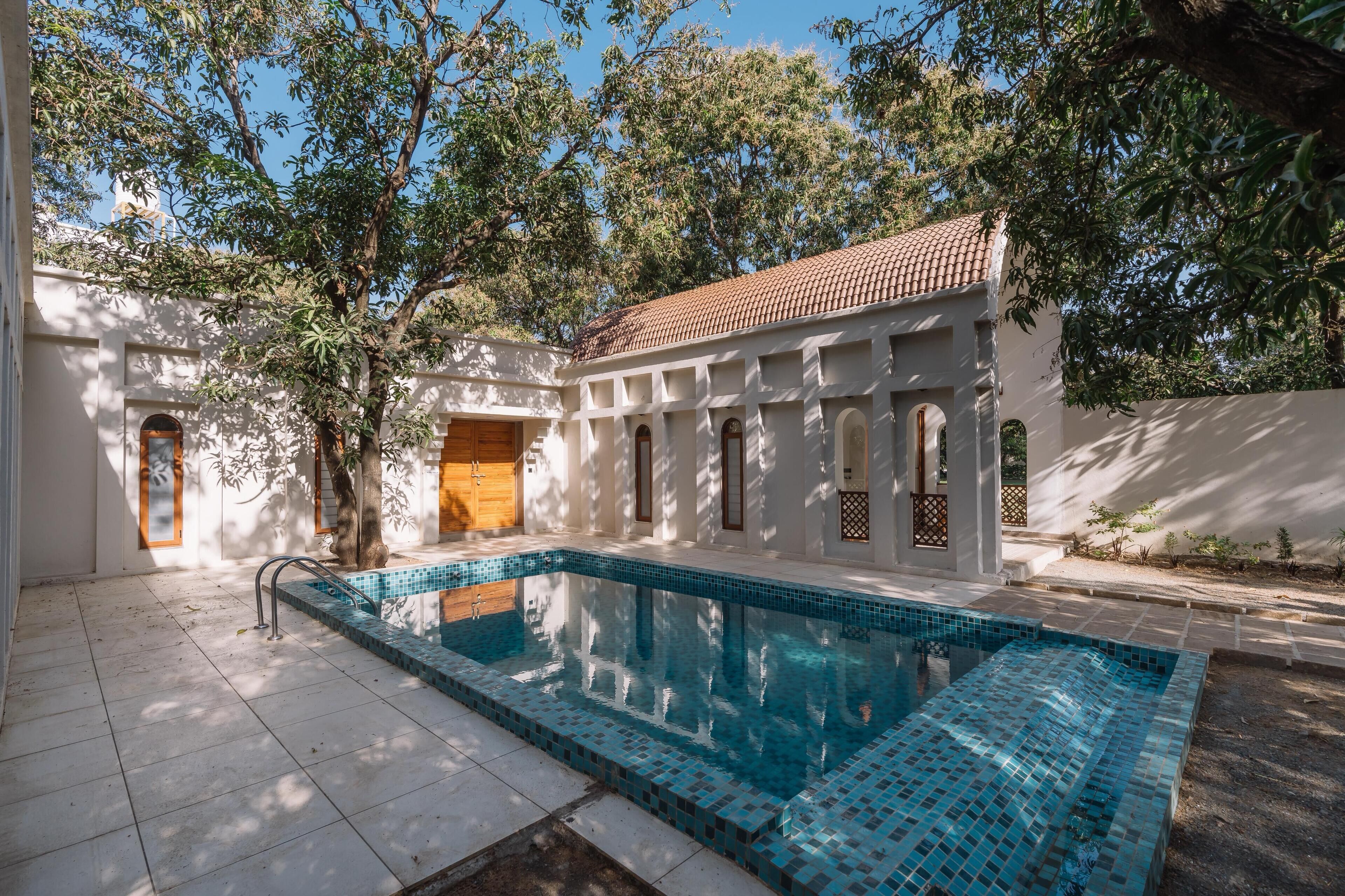 A swimming pool with tiled edges, surrounded by a white building with arched doorways and a tiled roof.