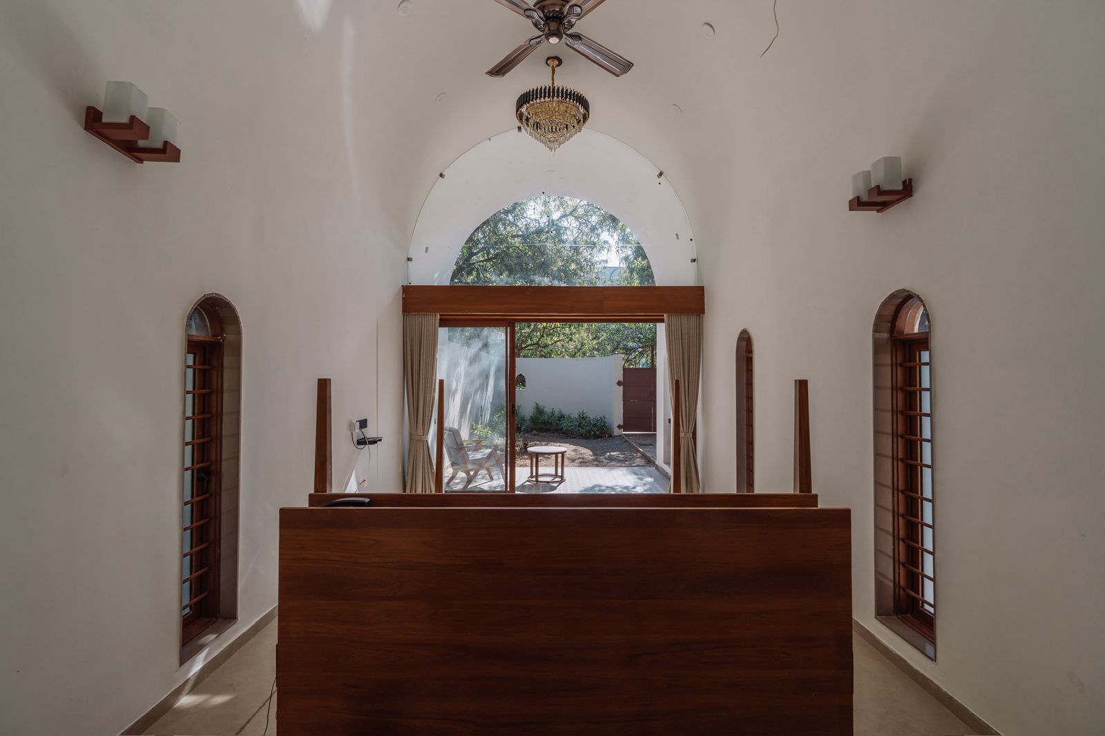 Um corredor com um banco de madeira, um ventilador de teto e vista para área externa com uma cadeira e uma mesa.