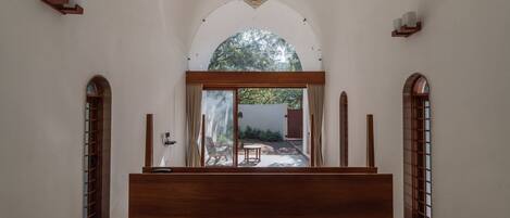 A corridor with a wooden bench, a ceiling fan, and a view of an outdoor area with a chair and a table.