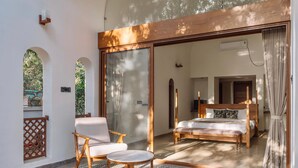 Une chambre dotée d’un grand lit, d’un coin salon avec un fauteuil et une table, et offrant une vue sur un balcon grâce à une porte vitrée.