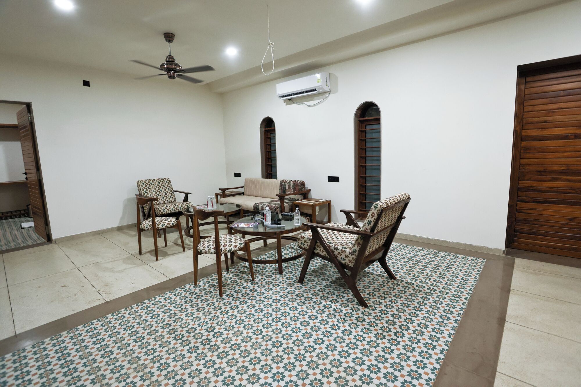 A spacious living room with a high ceiling fan, a sofa, two armchairs, a coffee table, and a patterned rug.