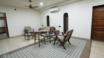 A spacious living room with a high ceiling fan, a sofa, two armchairs, a coffee table, and a patterned rug.