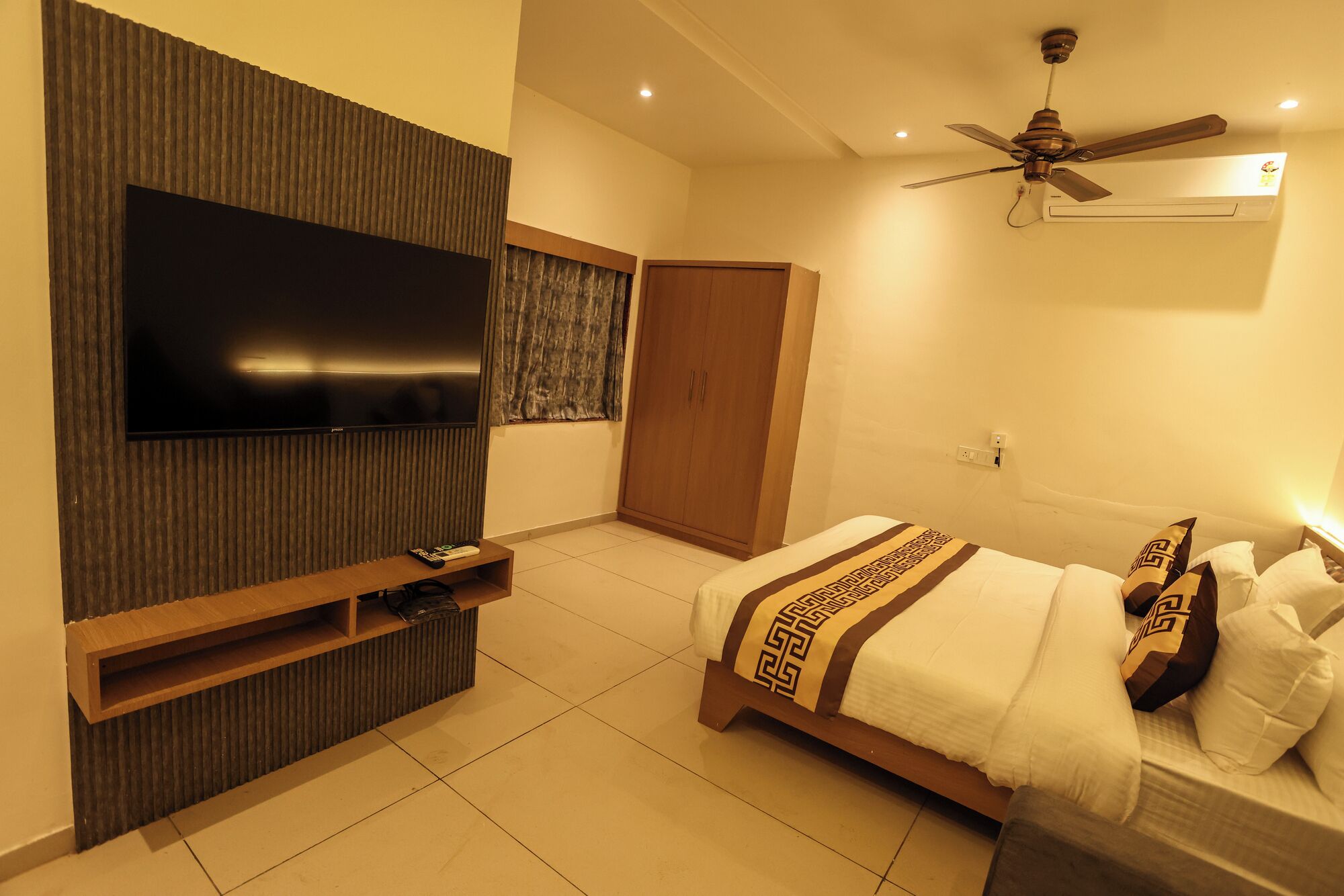 Ein Schlafzimmer mit Fernseher, Deckenventilator, Kleiderschrank und einem Bett mit gemusterten Bettbezügen.