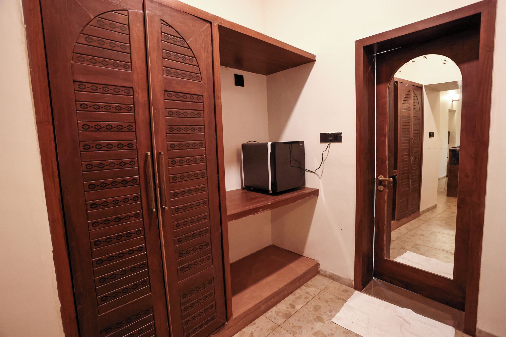 A hallway with a wooden door, a small shelf, and a mirror reflecting the door.