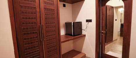 A hallway with a wooden door, a small shelf, and a mirror reflecting the door.