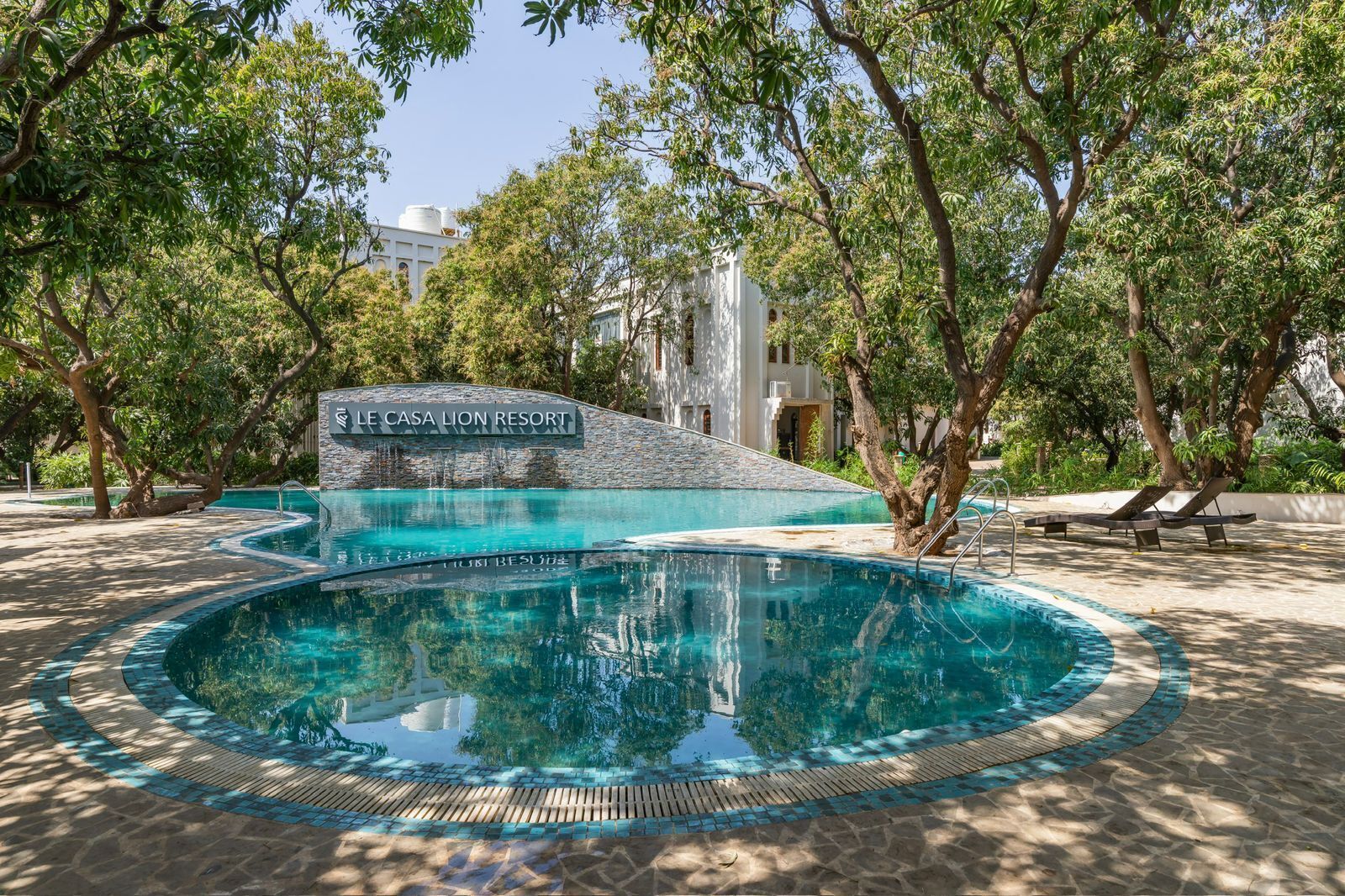 A swimming pool with a stone border, surrounded by trees and a sign reading "Le Casa Lion Resort".
