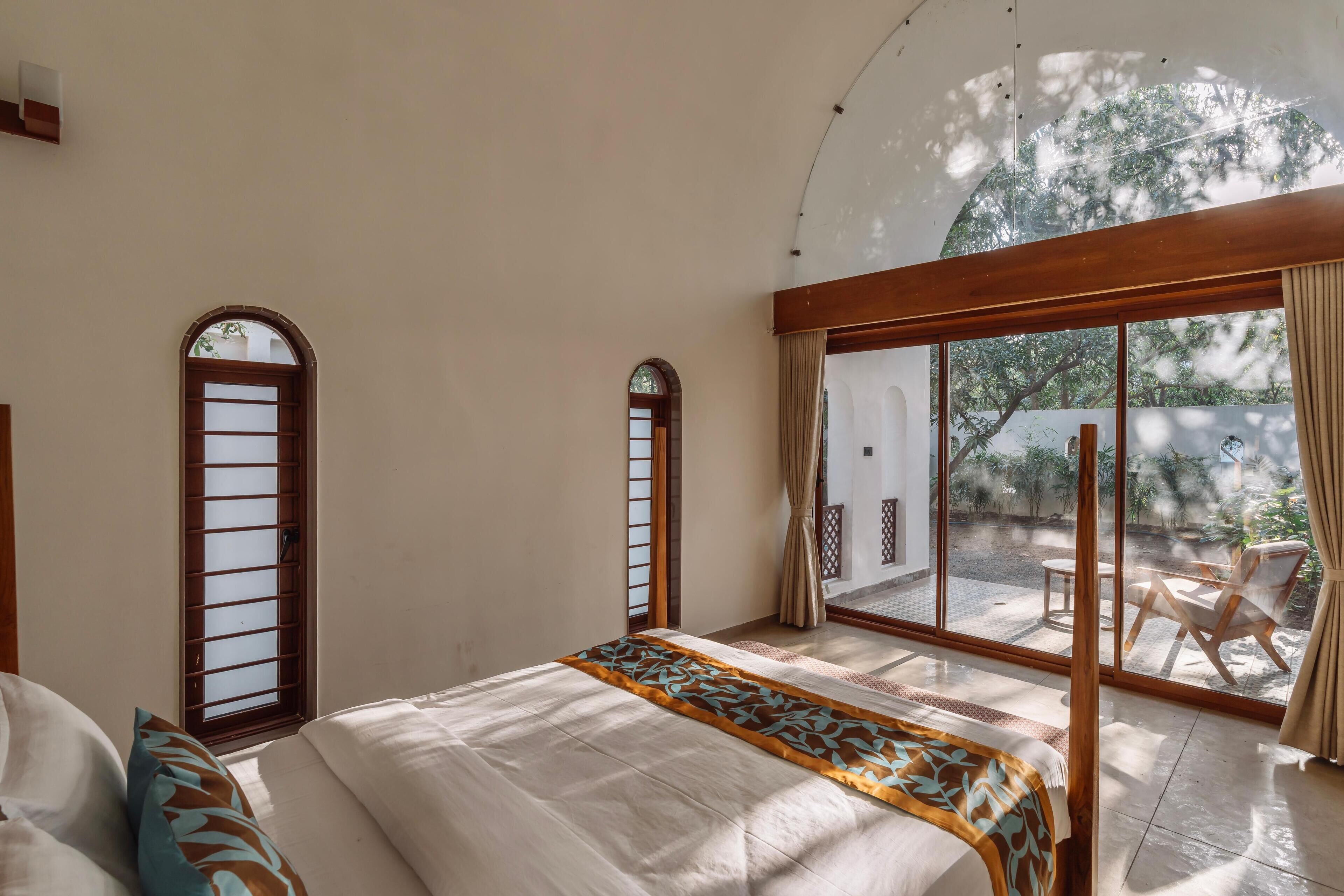 A bedroom with a large bed, two arched windows, and a view of a patio with outdoor furniture.