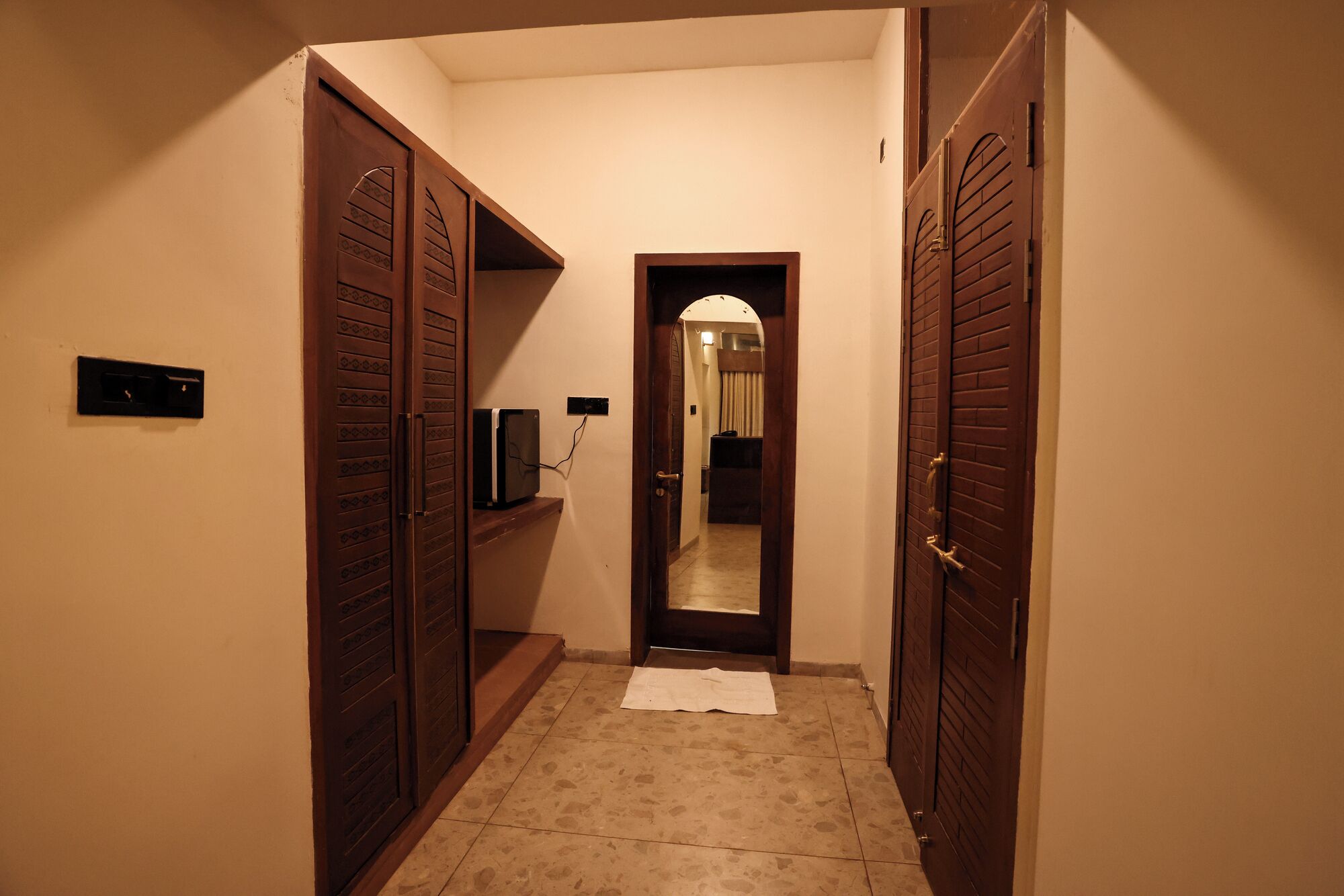 A narrow hallway with wooden doors on either side, a small shelf with a television, and a tiled floor.