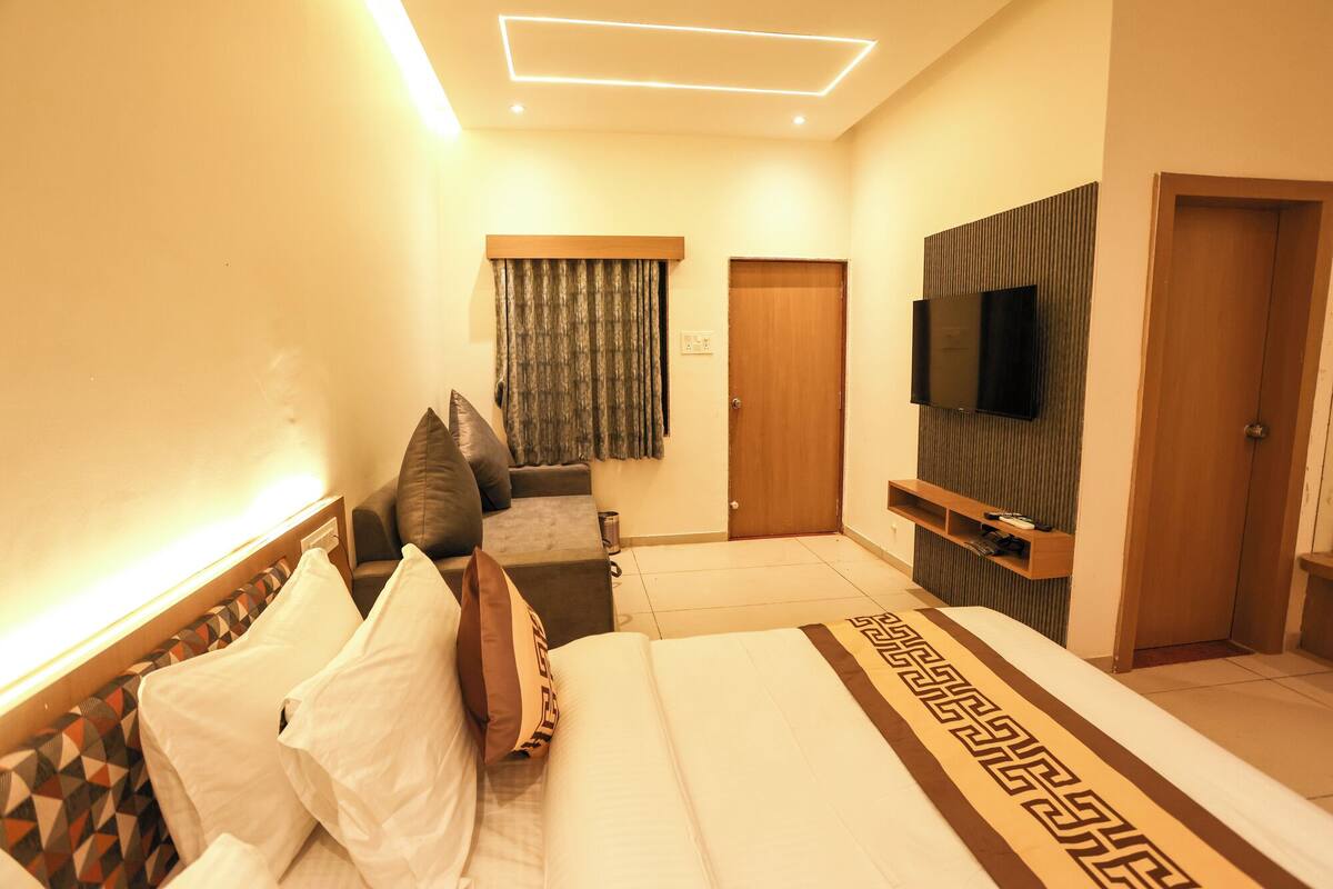 Quarto de hotel com cama, televisão na parede, sofá e porta.