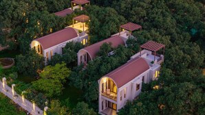 Un complexe hôtelier de luxe doté de plusieurs villas, chacune ayant un toit recouvert de tuiles rouges et étant entourée d’une végétation luxuriante.