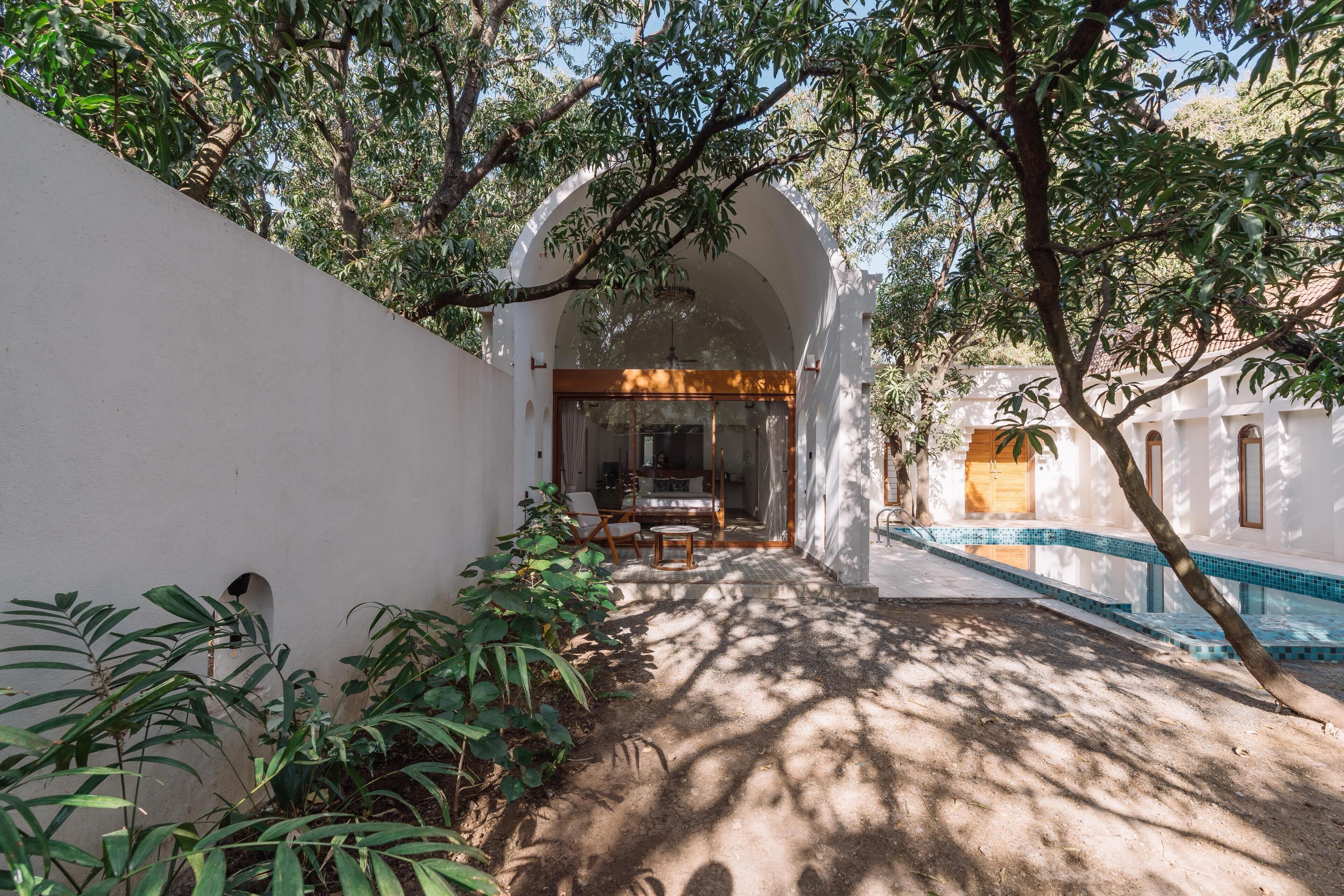 A covered outdoor area with a pool, surrounded by lush greenery and white walls.