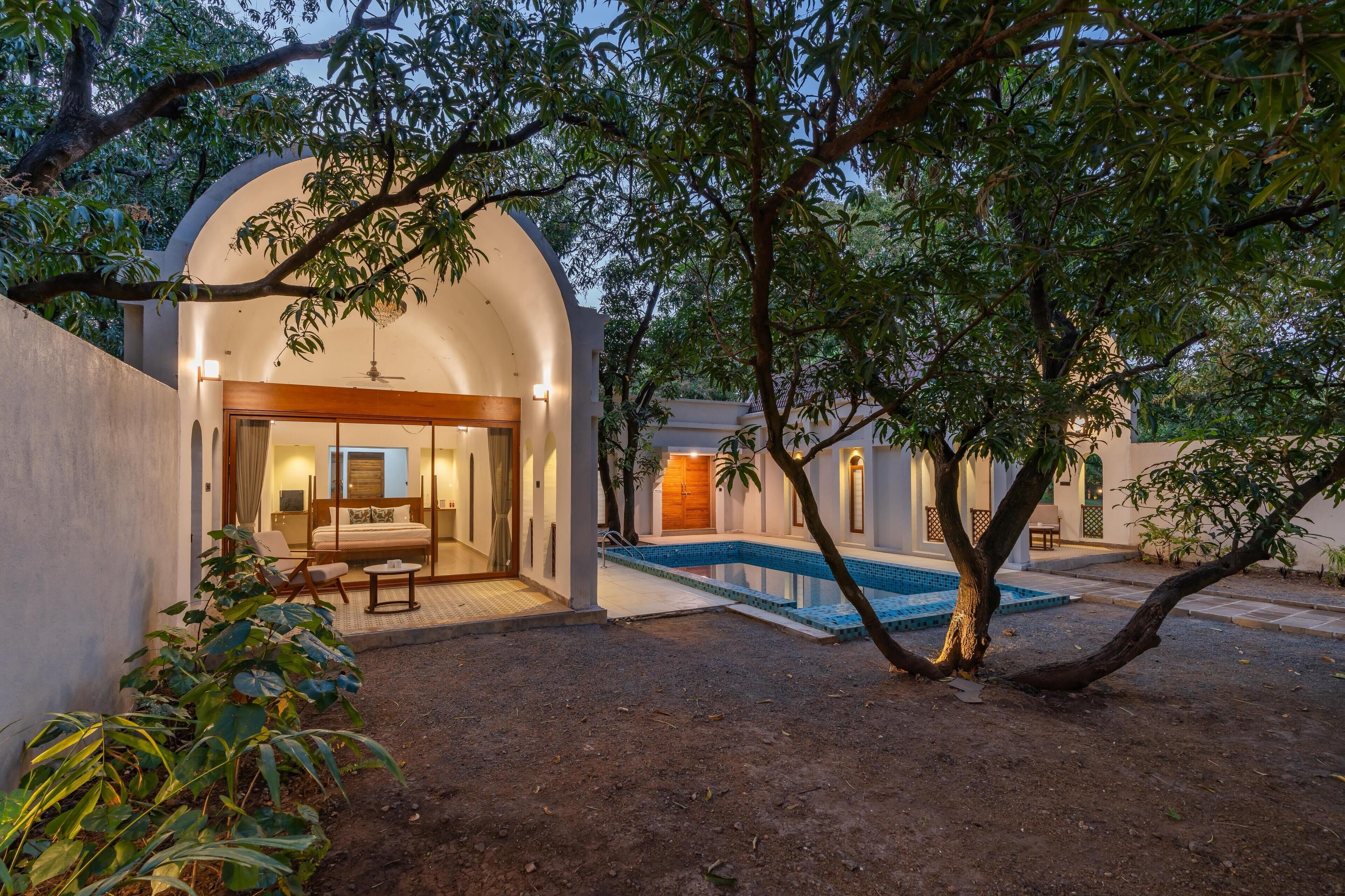 A villa with a swimming pool, a covered outdoor seating area, and a large tree in the foreground.