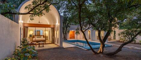 A villa with a swimming pool, a covered outdoor seating area, and a large tree in the foreground.