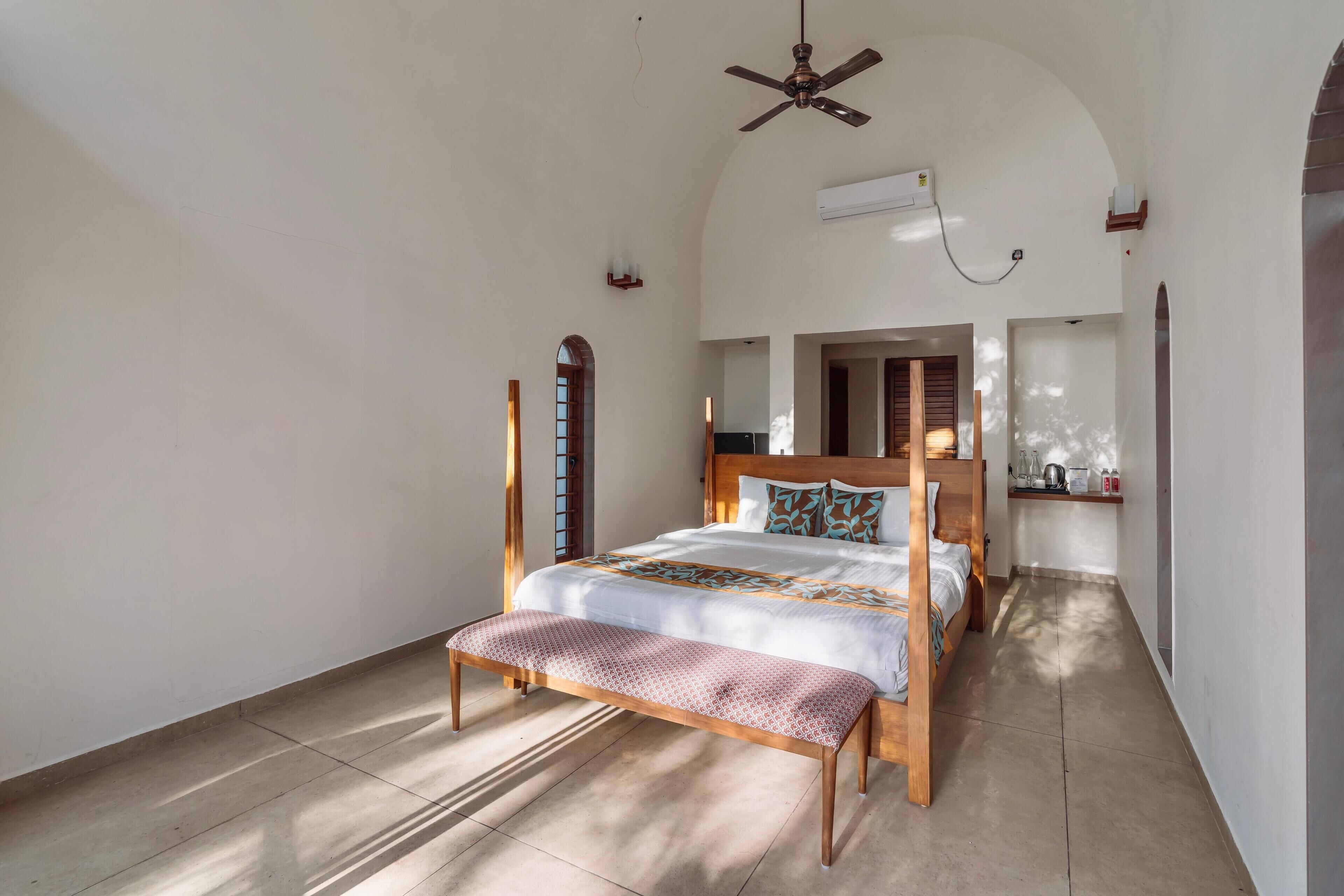 Un dormitorio espacioso con una cama grande, un banco de madera, un ventilador de techo y vistas al área de la cocina.