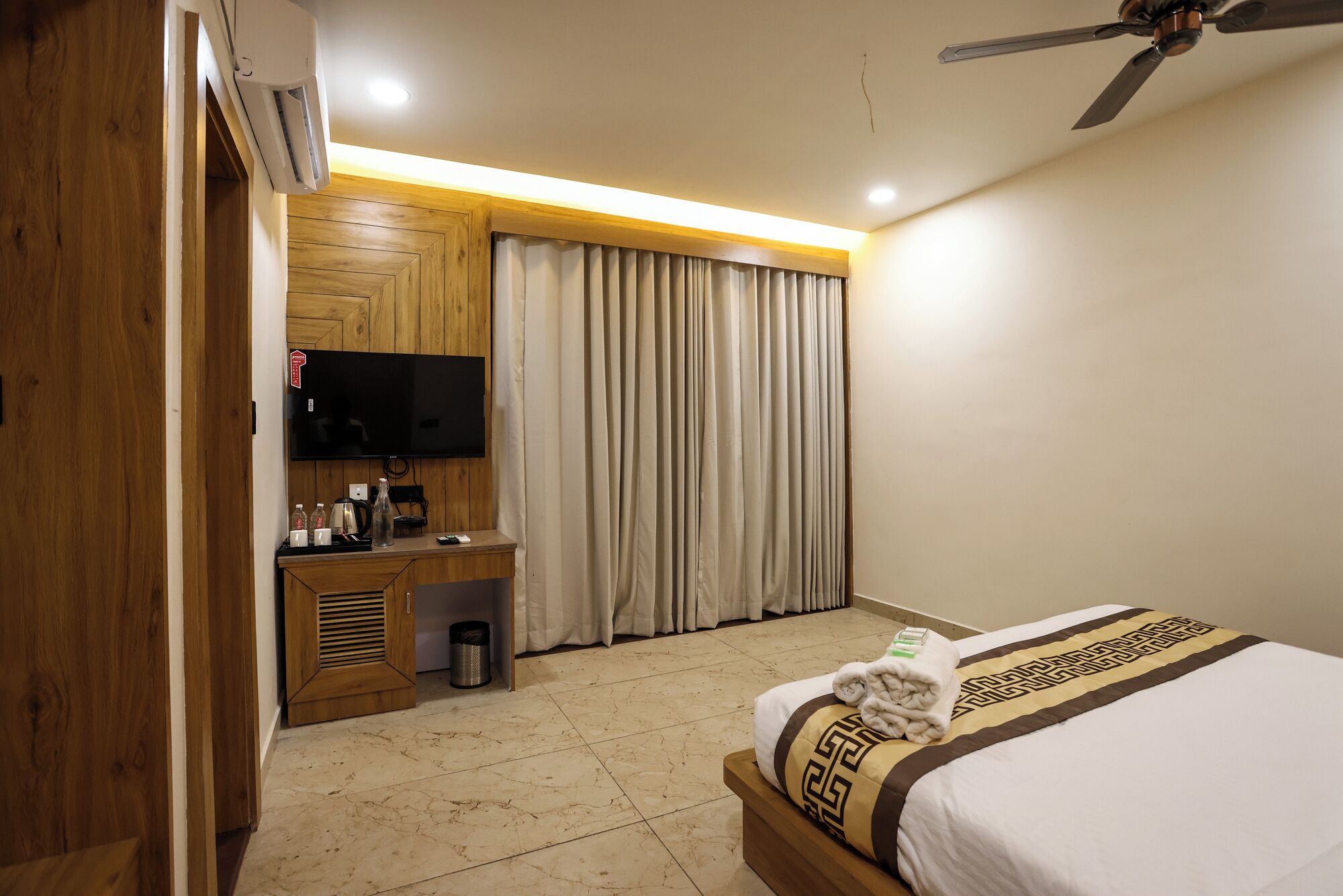 A hotel room with a bed, a desk, a television, and a ceiling fan.
