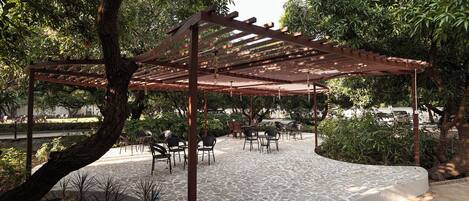 A covered outdoor seating area with stone flooring and wooden pergola.