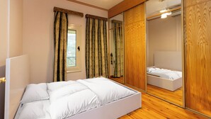 A bedroom with a bed, curtains, a mirror, and wooden flooring.